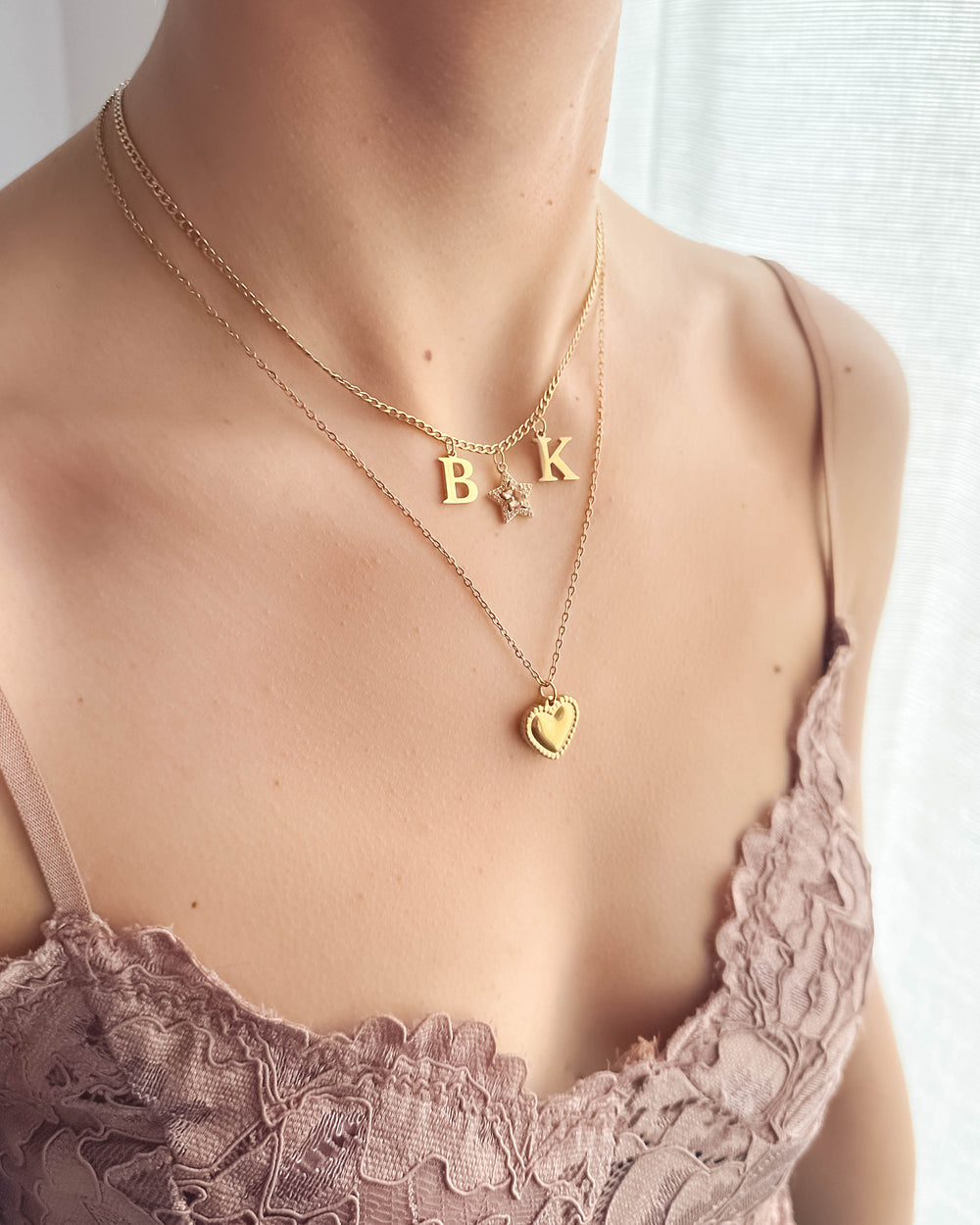 ras de cou charms initiales sur un cou accompagné d'un autre collier