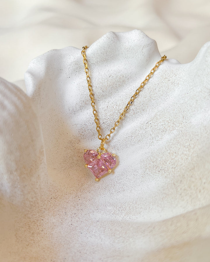 Collier cœur, pendentif rose posé sur une assiette coquillage
