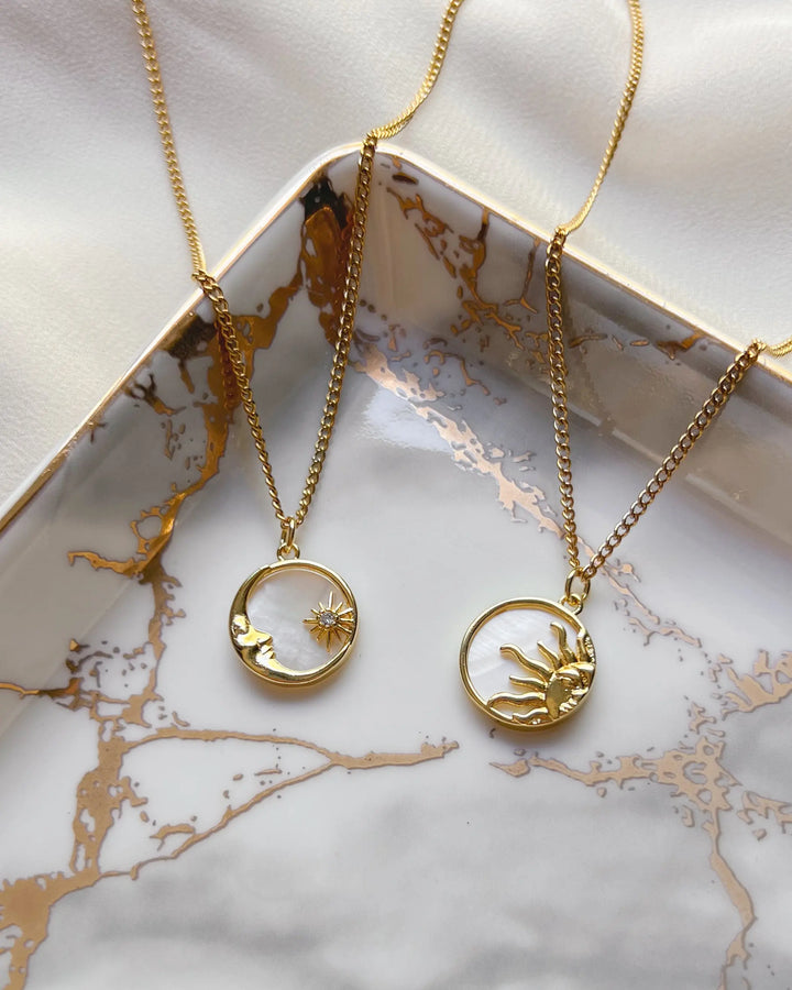 Duo de bijoux lune et soleil exposés sur une assiette blanche et dorée