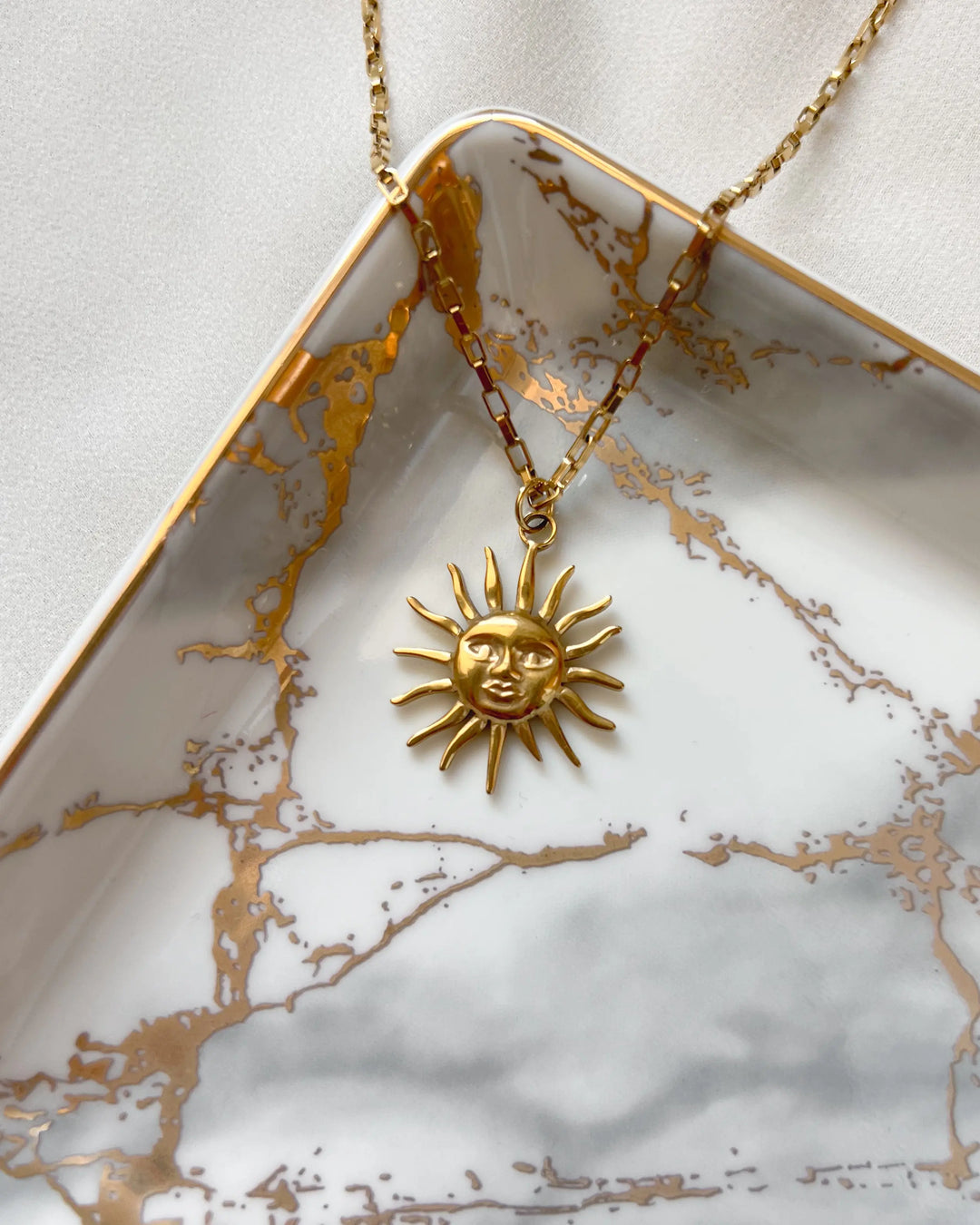 Pendentif soleil disposé sur une assiette blanche et dorée
