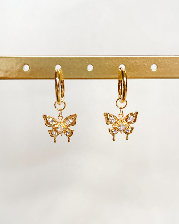 Boucles d'oreilles papillon sur un présentoir avec fond neutre.