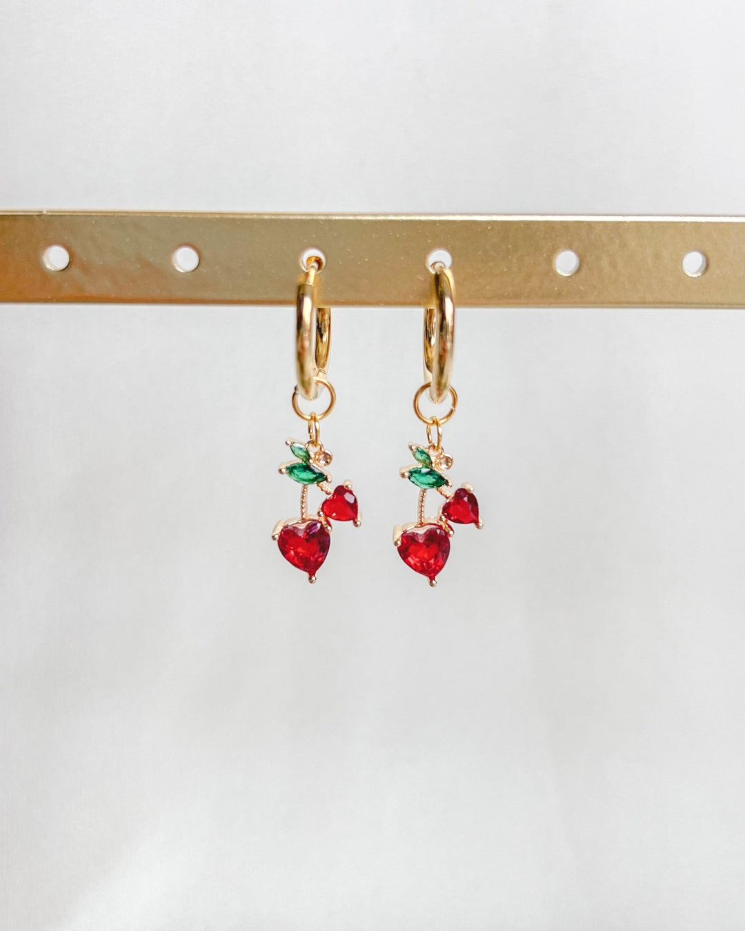 Boucles d'oreilles cerises sur un présentoir devant un fond neutre.