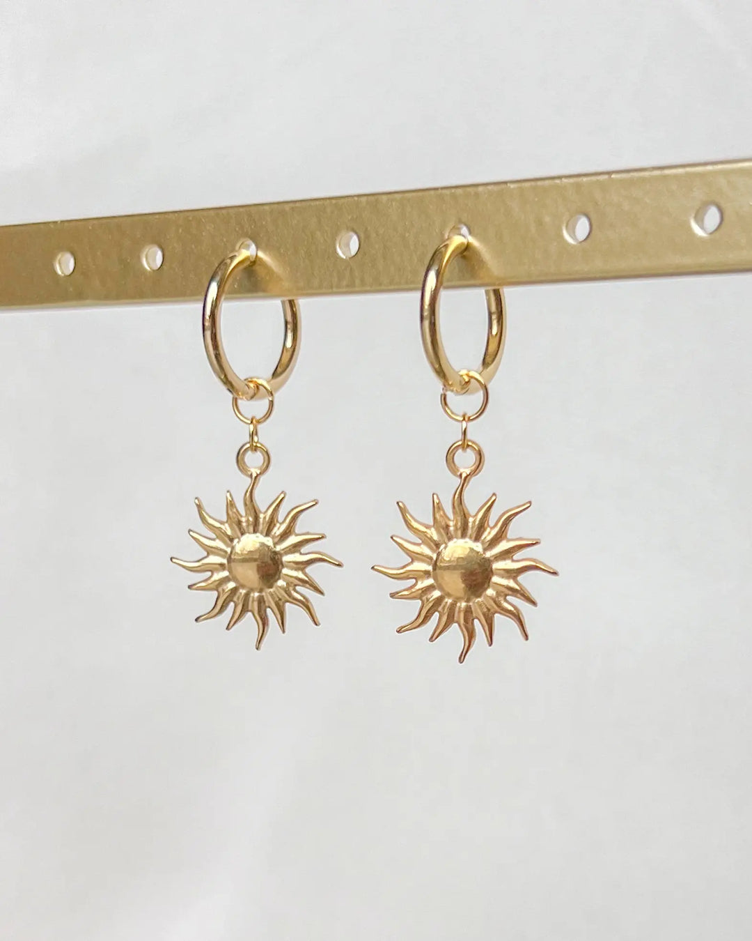 Boucles d'oreilles soleil sur fond neutre.