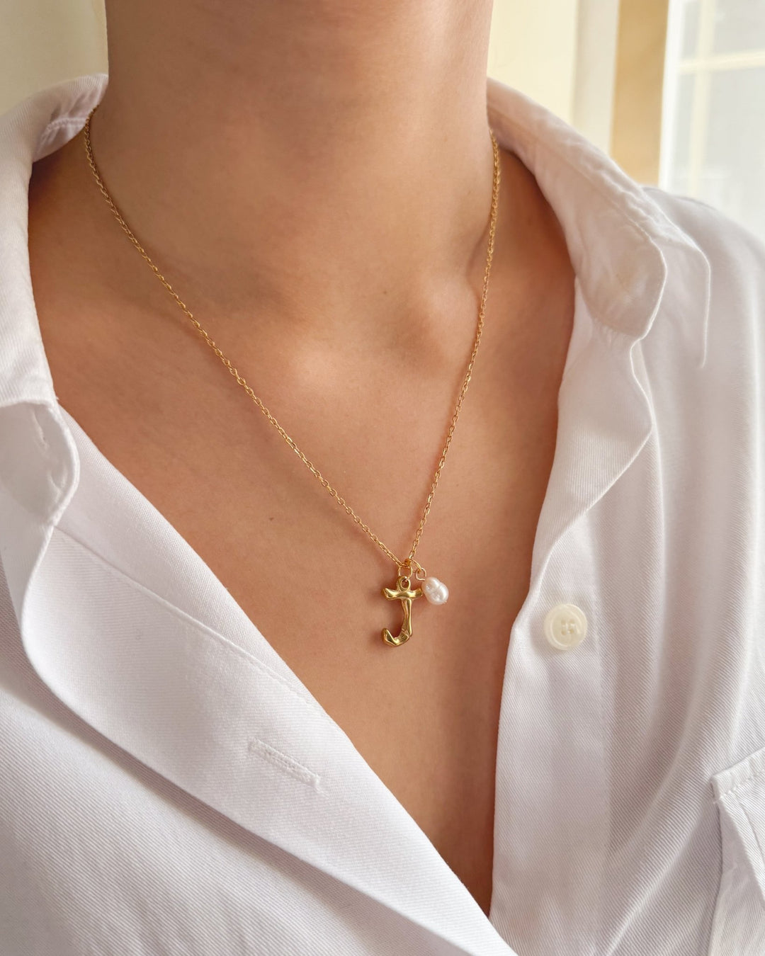 Collier initiale perle porté avec une chemise blanche.