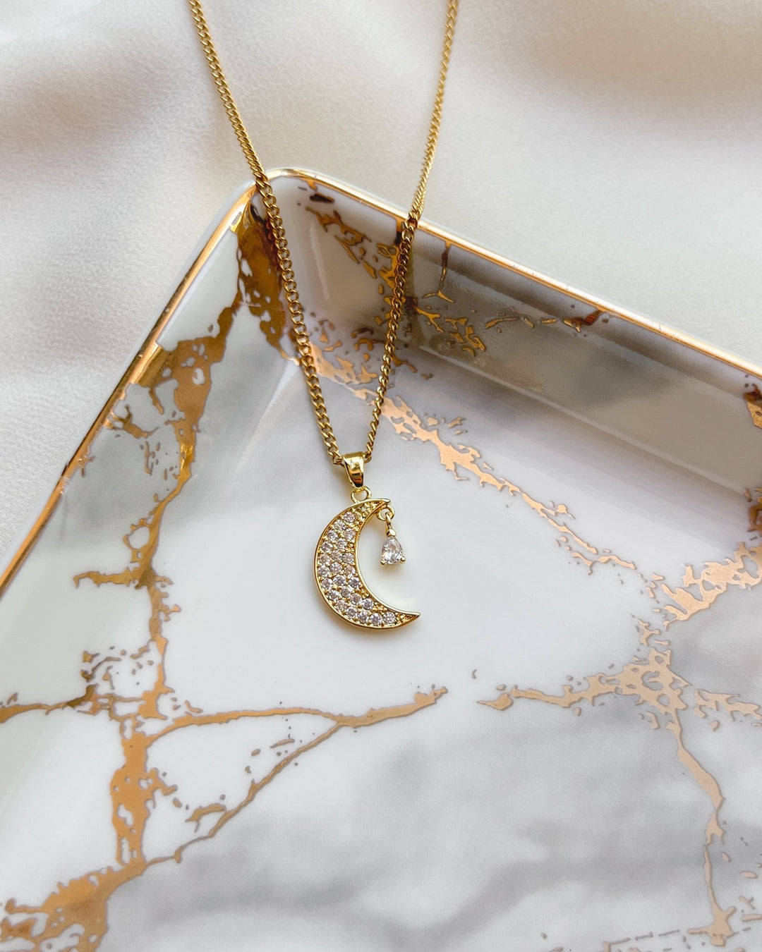 Collier croissant de lune sur une assiette blanche et dorée.